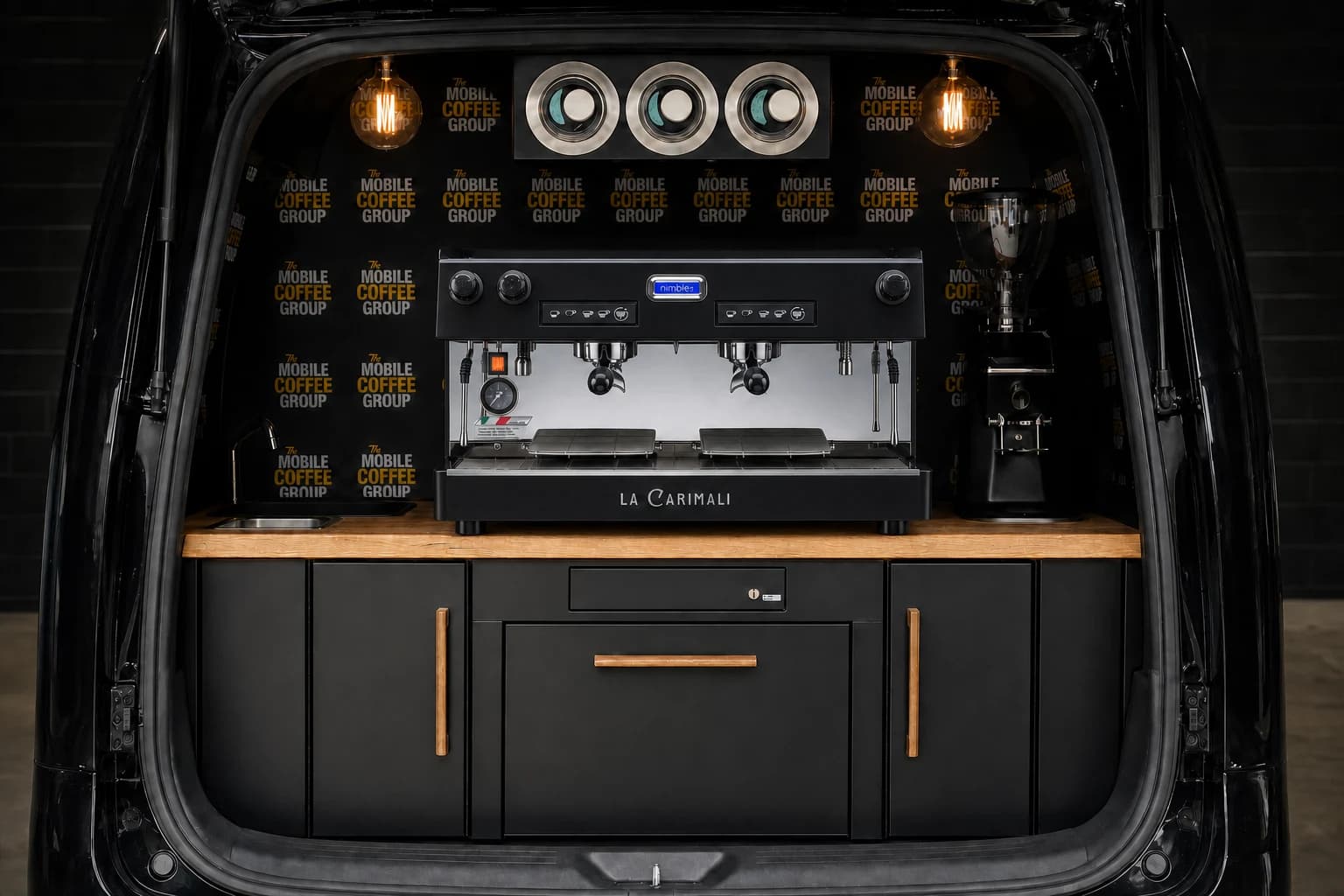 Universal Large Van Package visual with timber benchtop, black cabinetry, branded vinyl splashback and warm vintage lighting and a black Carimali Nimble espresso machine