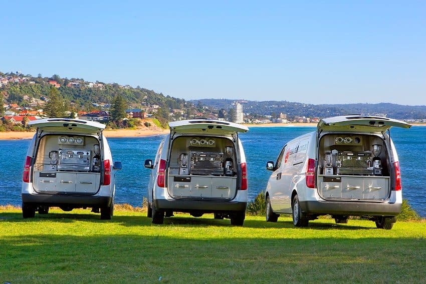 Three completed rear-service coffee vans beside the water
